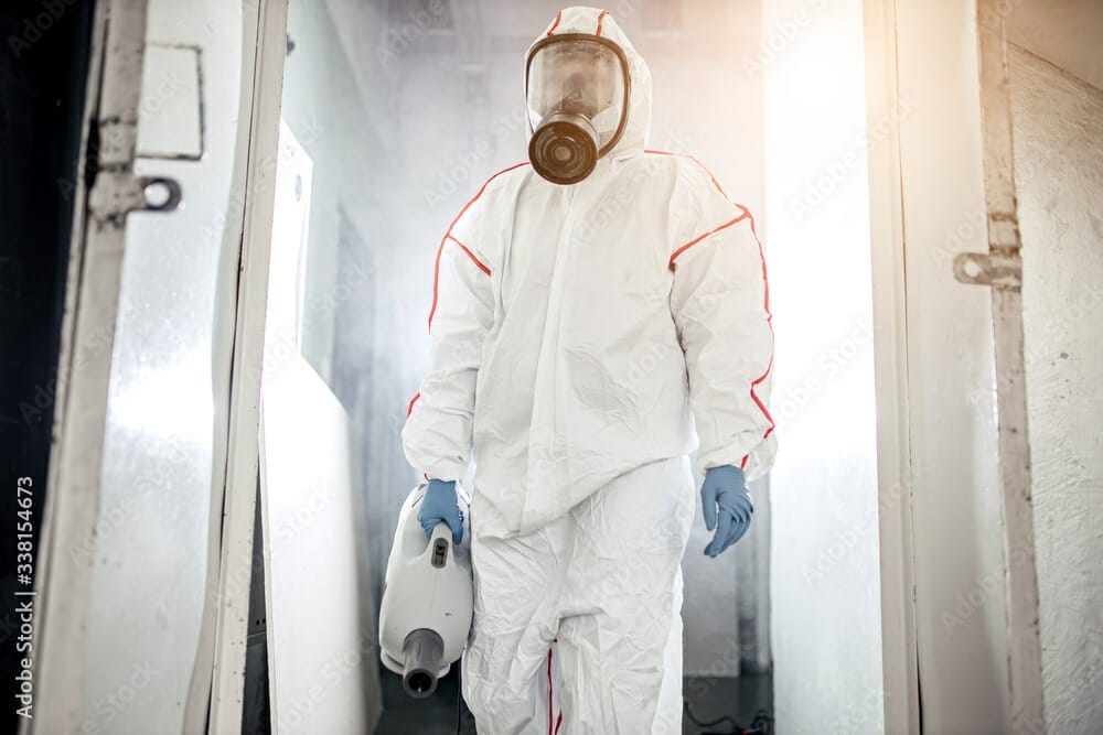 A firefighter in full gear sprays water on a burning building at night, with flames and smoke rising into the dark sky.