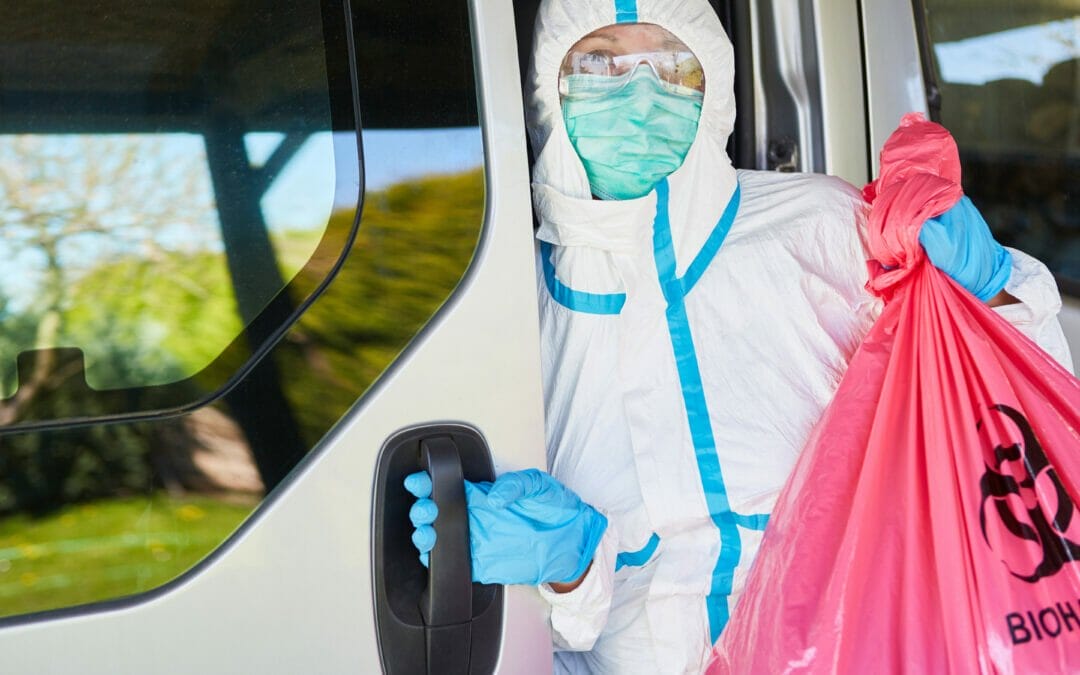 Cleaner in protective gear handling clinical waste during COVID-19 pandemic, emphasizing safe transport and disposal.